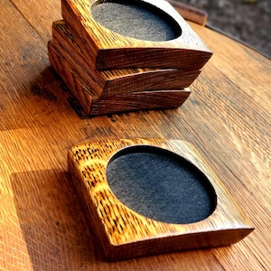 May include: Four brown wooden coasters with a round felt insert in the centre. The coasters are stacked on top of each other on a wooden surface.