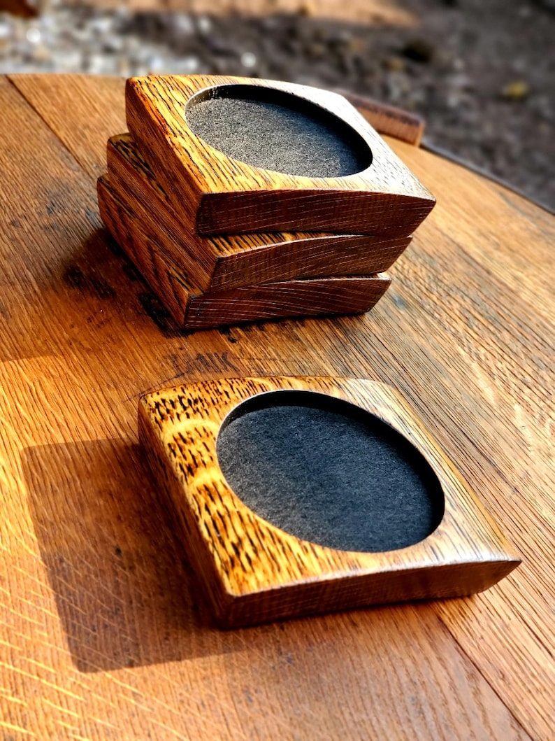 May include: Four brown wooden coasters with a round felt insert in the centre. The coasters are stacked on top of each other on a wooden surface.