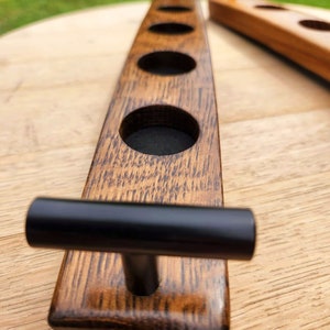 May include: A wooden beer caddy with four cup holders and black metal handles. The caddy is made from reclaimed wood and has a rustic finish.