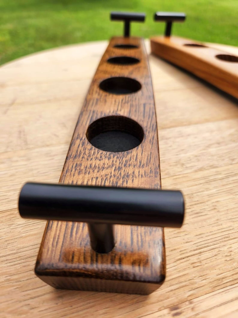 May include: A wooden beer caddy with four cup holders and black metal handles. The caddy is made from reclaimed wood and has a rustic finish.
