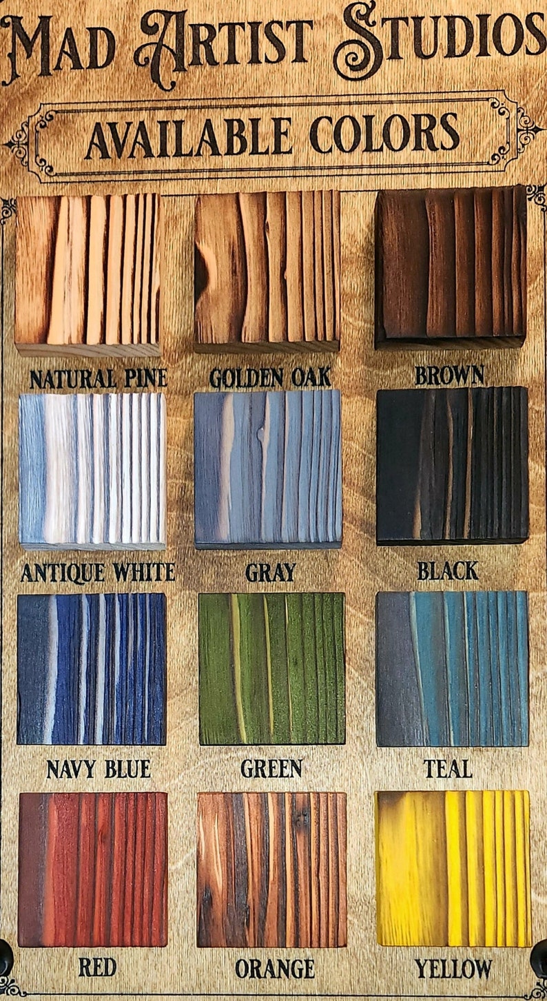 May include: A wooden sign with the text "MAD ARTIST STUDIOS" and "AVAILABLE COLORS" above a grid of 12 wood samples in different colors. The colors are: Natural Pine, Golden Oak, Brown, Antique White, Gray, Black, Navy Blue, Green, Teal, Red, Orange, and Yellow.