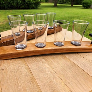 May include: A wooden shot glass holder with black metal handles and six clear glass shot glasses. The holder is made from reclaimed oak barrel staves.