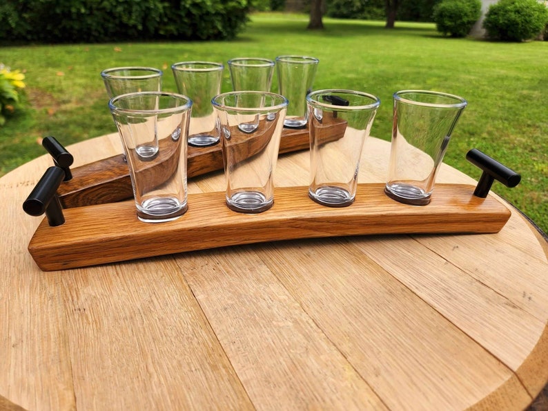 May include: A wooden shot glass holder with black metal handles and six clear glass shot glasses. The holder is made from reclaimed oak barrel staves.