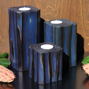 May include: Three blue and black wooden candle holders with white tea lights. The candle holders are made of wood and have a rustic look.