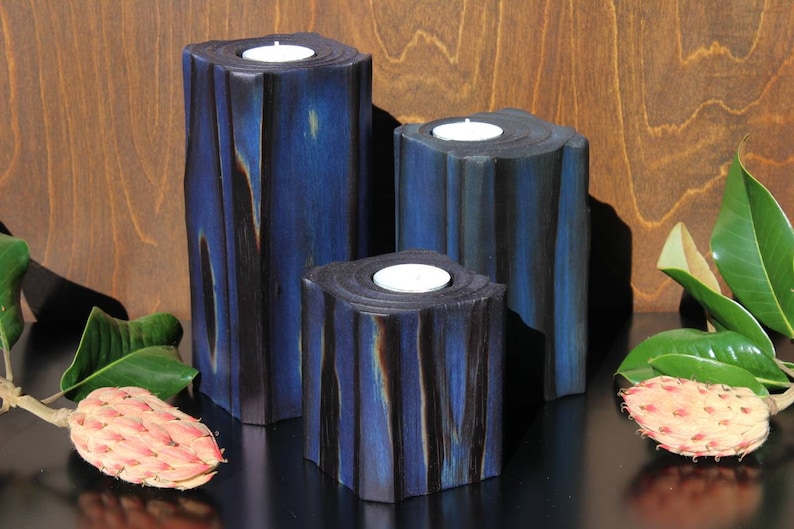 May include: Three blue and black wooden candle holders with white tea lights. The candle holders are made of wood and have a rustic look.