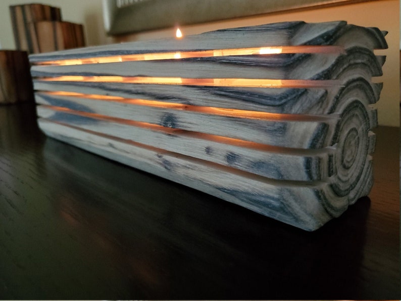 May include: A wooden candle holder with a natural wood finish and a gray stain. The holder has a series of slots that allow light from the candles to shine through. The holder is lit with several candles.