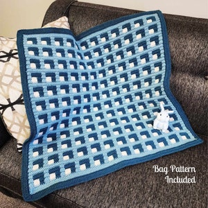 Op de afbeelding: Een gehaakte deken in blauw- en wittinten met een geometrisch patroon. De deken heeft een donkerblauwe rand en ligt op een bank. Een klein wit konijnbeeldje staat op de deken. De tekst "Bag Pattern Included" is zichtbaar.