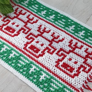 Könnte beinhalten: Ein weißer Häkelteppich mit roten und grünen Streifen. Der Teppich hat ein geometrisches Muster mit einem Fransenrand.