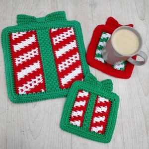 May include: Three crocheted Christmas gift-shaped coasters in green, red and white. The coasters are made with a simple stitch pattern and have a festive look.