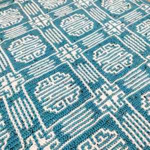 May include: A crocheted blanket with a geometric pattern in shades of teal and white.