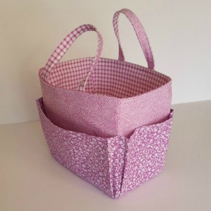 May include: A pink fabric storage basket with two handles and multiple pockets. The basket is lined with a pink and white gingham fabric.
