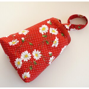 May include: A red fabric bag with white daisy flowers and white polka dots. The bag has a red ribbon handle with a knot.