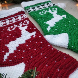May include: Two crocheted Christmas stockings with a reindeer design. One stocking is red with white accents and the other is green with white accents.