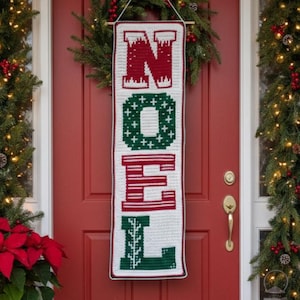 May include: A white, red, and green crochet banner with the word "NOEL" displayed vertically. The banner is hanging on a red door, with Christmas greenery and lights in the background. The letters are in a festive font.