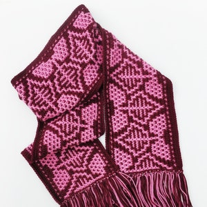 May include: A pink and burgundy crocheted scarf with a geometric pattern and fringe.