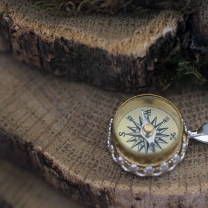 Peut inclure: Un collier avec un pendentif en forme de boussole dor&eacute;e et une cha&icirc;ne en argent. Le cadran de la boussole a des marques noires pour les points cardinaux et une aiguille en argent.