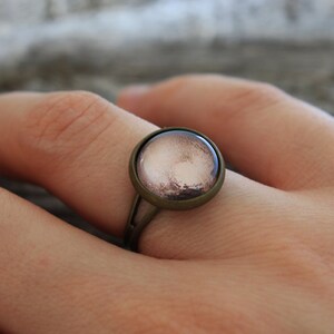 May include: A bronze ring with a round, glass cabochon featuring a brown and pink image of a planet.