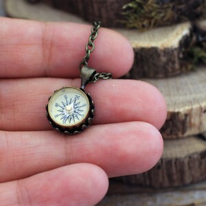Peut inclure: Un collier avec un pendentif en forme de boussole ronde en bronze. Le cadran de la boussole est blanc avec des marques noires et une aiguille dor&eacute;e.