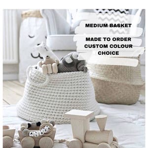Puede incluir: Una cesta de crochet blanca con animales de peluche dentro. La cesta est&aacute; etiquetada con "MEDIUM BASKET MADE TO ORDER CUSTOM COLOUR CHOICE". Un tren de juguete de madera est&aacute; en primer plano.
