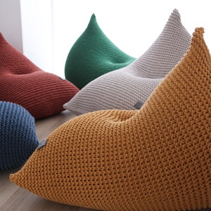 May include: Five knitted bean bags in different colours, including red, green, grey, blue, and yellow. The bags are all in a teardrop shape and have a textured knit pattern.