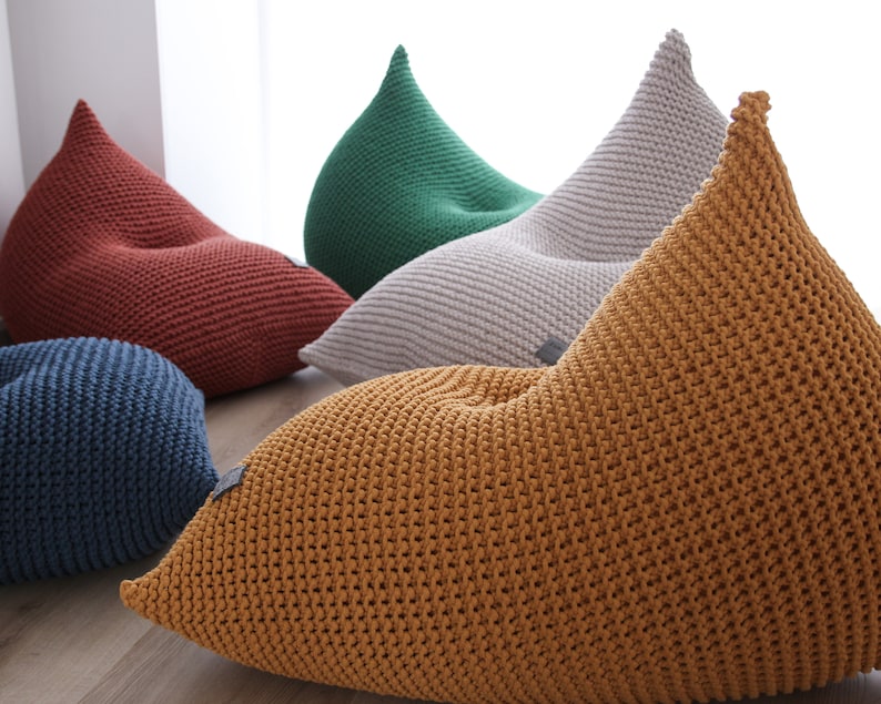 May include: Five knitted bean bags in different colours, including red, green, grey, blue, and yellow. The bags are all in a teardrop shape and have a textured knit pattern.