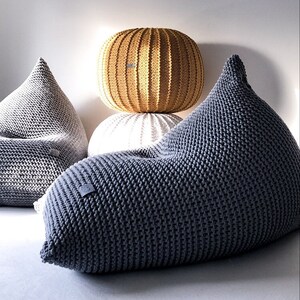 May include: Three knitted bean bags in grey, white and yellow. The bags are all made of a thick, textured yarn and have a relaxed, comfortable look.