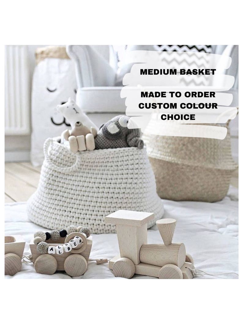 Puede incluir: Una cesta de crochet blanca con animales de peluche dentro. La cesta est&aacute; etiquetada con "MEDIUM BASKET MADE TO ORDER CUSTOM COLOUR CHOICE". Un tren de juguete de madera est&aacute; en primer plano.