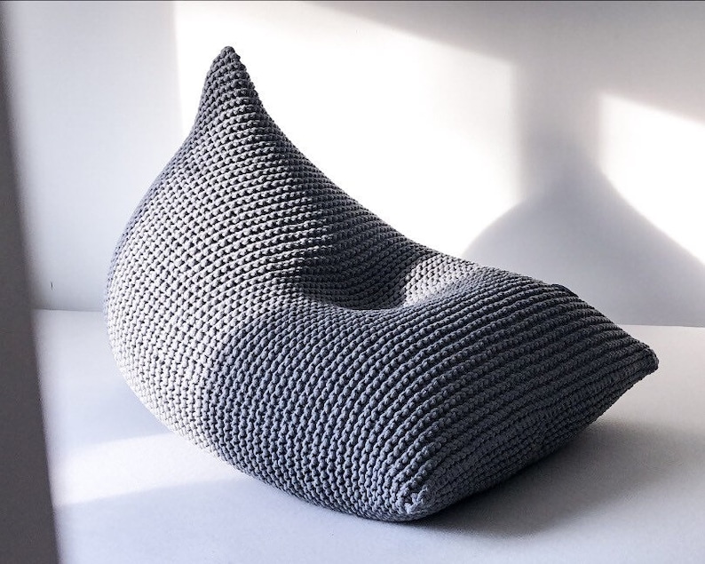 May include: A grey knitted beanbag chair with a unique teardrop shape. The chair is made of a soft, comfortable material and is perfect for relaxing.
