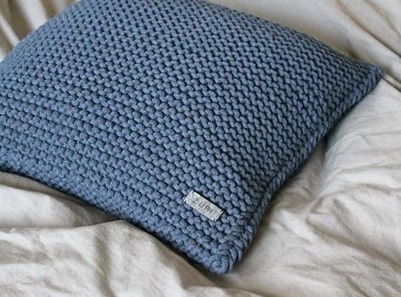 May include: A blue knitted throw pillow with a small white label that says "ZURI" on it.