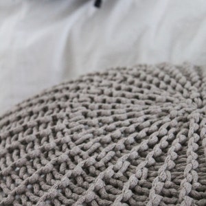 May include: Close-up of a grey knitted throw pillow with a textured, woven design.