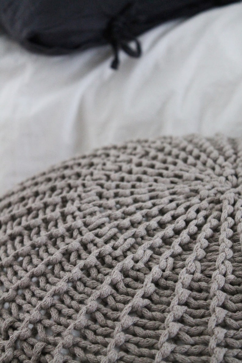 May include: Close-up of a grey knitted throw pillow with a textured, woven design.