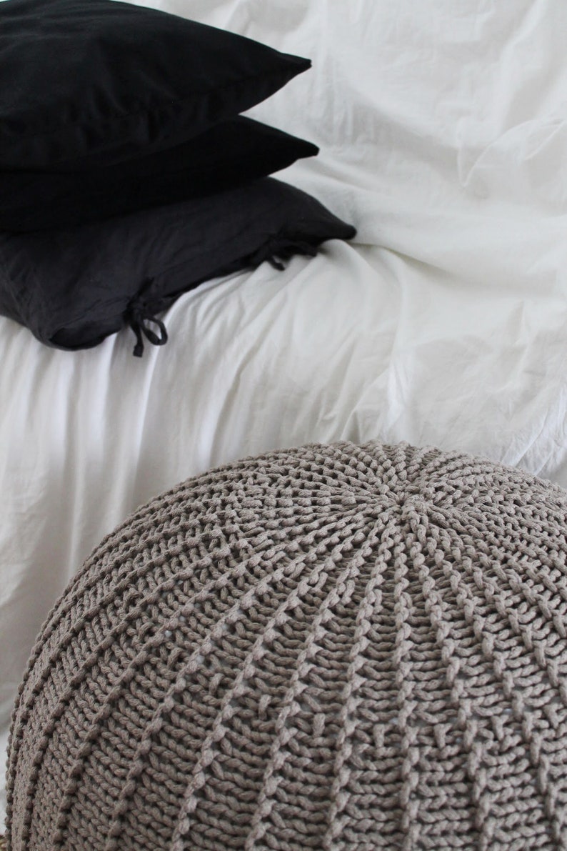 May include: A large, round, knitted pouffe in a light brown colour. The pouffe is made of thick, textured yarn and has a circular pattern.