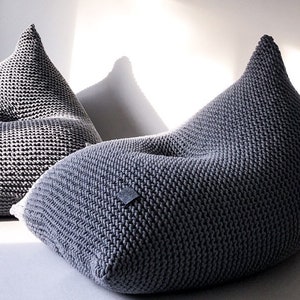 May include: Two grey knitted bean bag chairs. The chairs are made of a thick, textured fabric and have a rounded, comfortable shape.