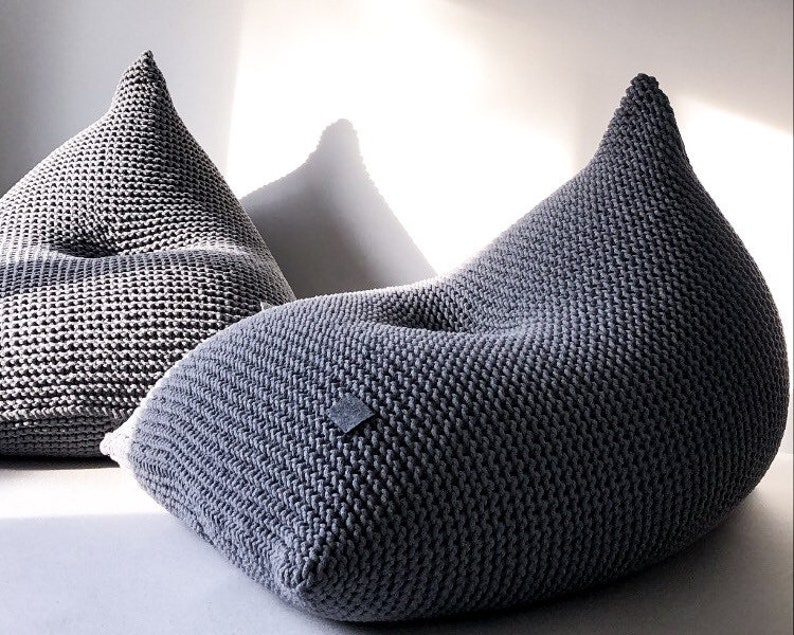 May include: Two grey knitted bean bag chairs. The chairs are made of a thick, textured fabric and have a rounded, comfortable shape.