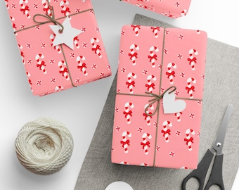 May include: Pink wrapped gifts with a candy cane pattern, tied with twine and white tags. A spool of twine, scissors, and additional tags are also present, suggesting a holiday theme.