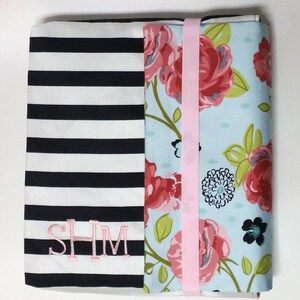 May include: A black and white striped fabric with a floral fabric panel sewn to it. The floral fabric has pink, blue, and green flowers on a light blue background. The striped fabric has the letters "SHM" embroidered on it in pink thread.