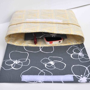 May include: A gray and yellow fabric pouch with a white zipper. The pouch is open and has a red pen, a black notebook, and a white phone inside. The pouch has a gray fabric lining with a white floral pattern.