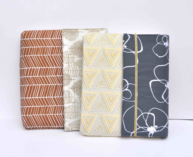 May include: Three fabric covered notebooks with different patterns. The first notebook has a brown and white chevron pattern. The second notebook has a white background with a brown leaf pattern. The third notebook has a gray background with a white floral pattern.