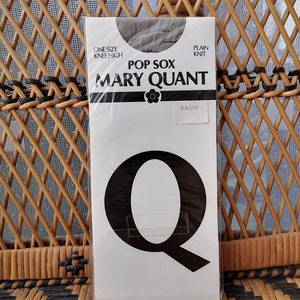 Op de afbeelding: Een verpakking Mary Quant Pop Sox kniekousen in de kleur fawn. De verpakking is wit met zwarte tekst en een zwarte bloemgrafiek. De tekst op de verpakking luidt "One Size Knee High", "Pop Sox", "Mary Quant", "Plain Knit" en "Fawn".