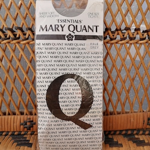 Op de afbeelding: Een verpakking 'Essentials' Mary Quant panty's in lichtgrijs, one size. De verpakking toont de merknaam, een bloemenlogo en de herhaalde tekst 'Mary Quant'. De woorden 'Sheer Soft and Smooth' zijn ook zichtbaar.