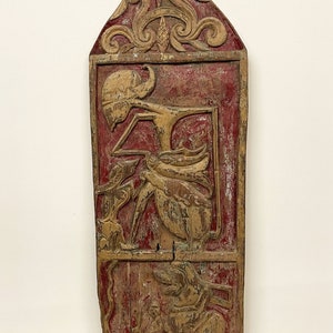 May include: A carved wooden panel with a red background and gold accents. The panel features intricate carvings of figures and floral designs.