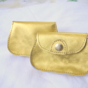 May include: Two gold leather coin purses with a button closure. The smaller purse has a flap with a button closure.