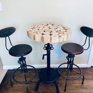 May include: A round wooden table with a unique log slice top, surrounded by two black metal bar stools with brown seats. The table and stools have a rustic industrial style.