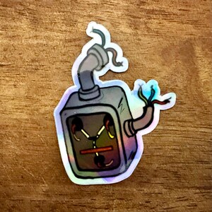 May include: A holographic sticker of a gray and silver futuristic device with wires and a glowing green screen. The sticker is on a wood background.