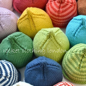 May include: A collection of colourful knitted hats in various patterns and colours, including red, yellow, green, blue, and white. The hats are all made with a similar stitch pattern and have a pointed top. The text "rocketclothing london" is visible in the image.