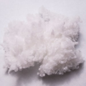 K&ouml;nnte beinhalten: Nahaufnahme einer wei&szlig;en, flauschigen, synthetischen F&uuml;llfaser. Die Faser ist locker und scheint aus kleinen, einzelnen Str&auml;hnen zu bestehen.