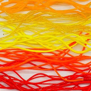 May include: A close-up of a collection of colorful, thin, flexible cords. The cords are arranged in layers, transitioning from red at the bottom to orange, yellow, and finally, a lighter orange at the top. The cords appear to be made of a shiny, plastic-like material.
