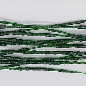 May include: Close-up of several strands of dark green, textured material, possibly decorative or craft supplies. The strands are arranged horizontally against a white background, creating a pattern of parallel lines. The material appears to have a slightly rough, uneven surface.