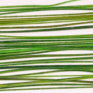 May include: A collection of green glass rods, arranged in rows on a white surface. The rods are approximately 1/4 inch in diameter and vary in length.