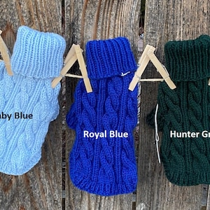 May include: Five knitted dog sweaters hanging on a clothesline. The sweaters are in the colours navy, baby blue, royal blue, hunter green, and mint.